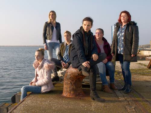 Sechs Frauen auf einer Straße am Meer.